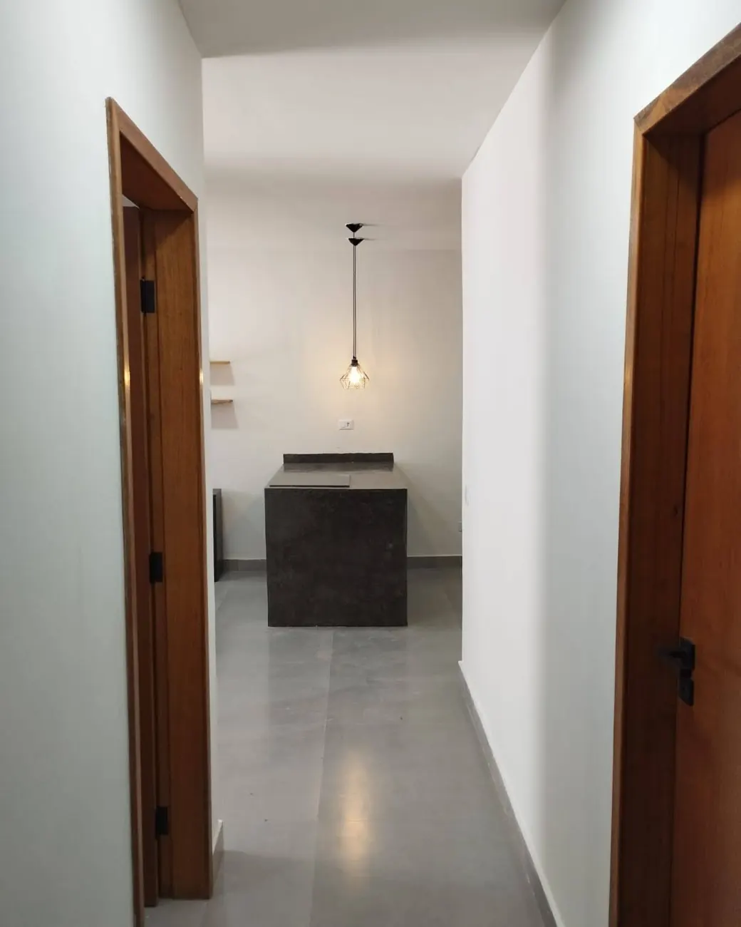 Corredor de uma casa entregue pela MV, com portas de madeira e a cozinha ao fundo
